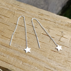 May include: A pair of silver star-shaped dangle earrings with a chain and a straight bar hanging from each star.