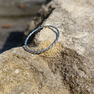 May include: A silver twisted band ring. The ring is on a light brown rock.