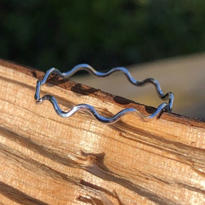 May include: A silver wavy ring, made of thin metal, is resting on a piece of wood.