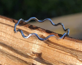 May include: A silver wavy ring, made of thin metal, is resting on a piece of wood.