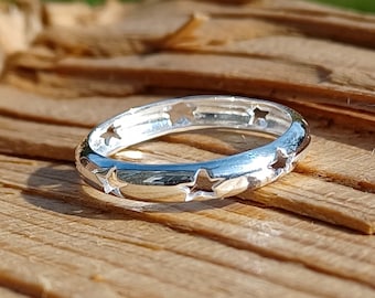 May include: A silver ring with a star cut-out design. The ring is on a wooden surface.