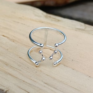 Op de afbeelding: Een zilveren ring met een dubbelband ontwerp. De bovenste band heeft een verticale balk en de onderste band heeft een sterrenbeeld ontwerp met kleine ronde kralen.