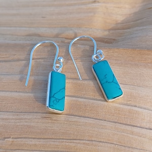 May include: A pair of silver dangle earrings with turquoise stones. The stones are rectangular and have a marbled pattern.