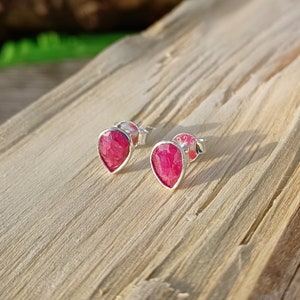 May include: A pair of silver stud earrings with teardrop-shaped pink gemstones.
