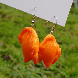 Könnte beinhalten: Ein Paar orangefarbene Hähnchenschenkel-Ohrringe. Die Ohrringe sind aus einem glänzenden, glatten Material gefertigt und haben silberne Haken.