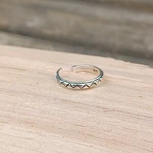 May include: A silver toe ring with a geometric design. The ring is made of sterling silver and has a simple, elegant design.