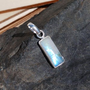 Peut inclure: Un pendentif rectangulaire avec un cadre argenté et une pierre irisée. La pierre affiche des couleurs bleues et blanches. Le pendentif est conçu pour un collier.