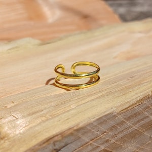 May include: A gold-toned double band ring with a simple design. The ring is made of two thin bands that are joined together at the top.