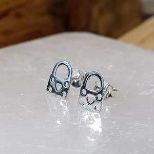 May include: A pair of silver padlock earrings with a heart cutout detail.