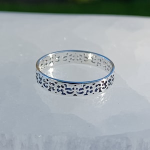Peut inclure: Une bague en argent avec un design délicat et complexe. La bague est faite d'une bande fine avec un motif découpé qui ressemble à un motif floral.