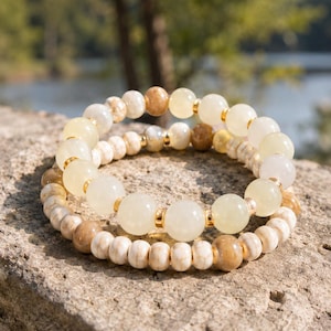 May include: Two stacked bracelets featuring smooth, round, translucent pale yellow beads and smaller, textured, off-white and tan marbled disc beads. The bracelets are accented with small, polished gold-tone metal spacers between the beads.
