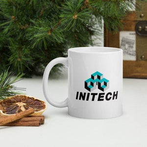 May include: White ceramic mug with a black and teal logo that says "INITECH". The logo features a stylized design of three stacked cubes.