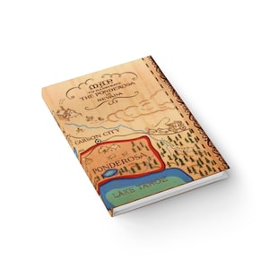 May include: A rectangular notebook with a light wood-grain cover featuring a printed map titled Map to Illustrate The Ponderosa in Nevada. The map displays Carson City, Lake Tahoe, and the Ponderosa area with illustrated trees, a stagecoach, and buildings.