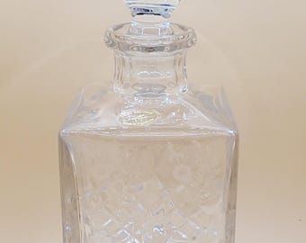 May include: A clear glass decanter with a square body and a faceted design. The decanter has a round, faceted stopper.