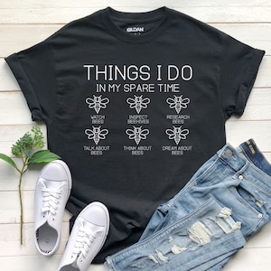 May include: Black t-shirt with white text that reads "Things I do in my spare time" and six bee illustrations with text below each bee that reads "Watch Bees", "Inspect Beehives", "Research Bees", "Talk About Bees", "Think About Bees", and "Dream About Bees".