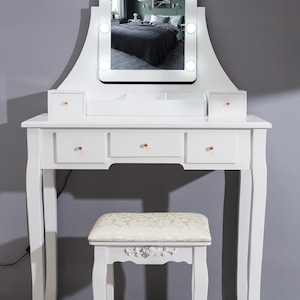 May include: A white dressing table with a lighted mirror, three drawers, and two small side drawers. The vanity has a matching stool with a patterned cushion. The mirror is surrounded by lights. The vanity table is 122 cm wide.