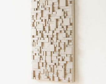 May include: A rectangular, off-white wall art piece with a 3D geometric design. The artwork features an arrangement of varying-sized, protruding rectangular blocks, creating a textured surface. The piece is mounted on a white wall.