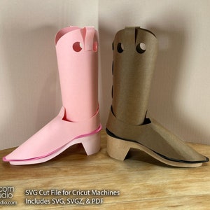 May include: Two papercraft cowboy boots, one pink and one brown, with a black outline around the sole. The boots are sitting on a wooden surface.