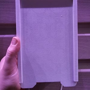May include: A white plastic wall plate with two holes at the bottom and a white cord attached.