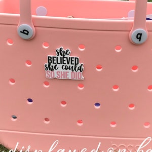 May include: A pink tote bag with a white handle and a black charm that says "She Believed She Could So She Did".