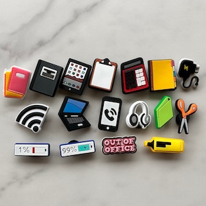 May include: A set of 15 colorful office-themed shoe charms, including a laptop, phone, calculator, notepad, scissors, and a power cord. The charms are made of rubber and have a glossy finish.