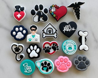 May include: A collection of 17 colorful and black and white charms featuring paw prints, hearts, dog bones, and other dog-themed designs. The charms are made of silicone and are perfect for adding a touch of personality to your shoes, bags, or other accessories.