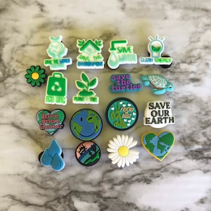 May include: A set of 15 colorful shoe charms with environmental themes. The charms feature images of a lightbulb, a plant, a turtle, a heart, a daisy, a water droplet, a globe, and a recycling bin. The charms also include text such as "Save the World", "Save the Environment", "Save Water", "Clean Energy", "Save the Turtles", "Eco Bag", "Plant a Tree", "Love Your Mother", "Friend Bugs", and "Save Our Earth".