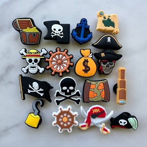 May include: A set of 16 colorful pirate-themed shoe charms. The charms include a treasure chest, skull and crossbones, anchor, map, pirate hat, steering wheel, money bag, telescope, hook, sword, and more.