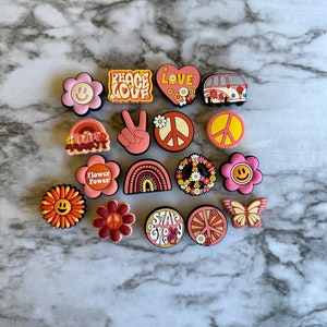 May include: A collection of 15 colorful, retro-style charms featuring peace signs, flowers, rainbows, and the words "Peace Love", "Flower Power", "Stay Groovy", and "Love".
