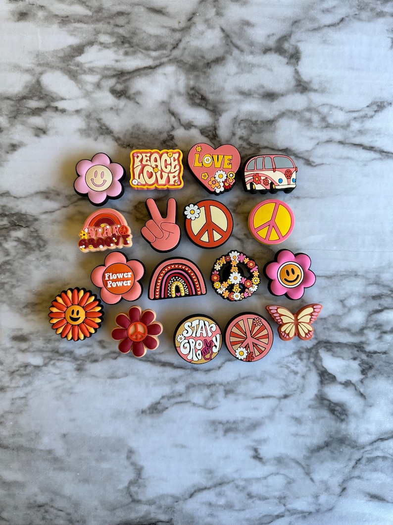 May include: A collection of 15 colorful, retro-style charms featuring peace signs, flowers, rainbows, and the words "Peace Love", "Flower Power", "Stay Groovy", and "Love".
