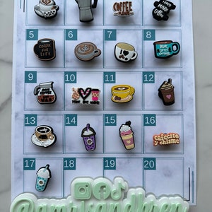 Op de afbeelding: Een wit bord met een raster van 20 vierkanten, elk met een andere koffie-thema charme. De charmes zijn gemaakt van siliconen en hebben verschillende ontwerpen, waaronder koffiekopjes, koffiebonen en koffiezetapparaten. Het bord is bovenaan gelabeld met "Amris & Bren" en onderaan met "@amrisandbren".
