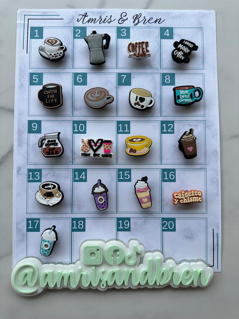 Op de afbeelding: Een wit bord met een raster van 20 vierkanten, elk met een andere koffie-thema charme. De charmes zijn gemaakt van siliconen en hebben verschillende ontwerpen, waaronder koffiekopjes, koffiebonen en koffiezetapparaten. Het bord is bovenaan gelabeld met "Amris & Bren" en onderaan met "@amrisandbren".