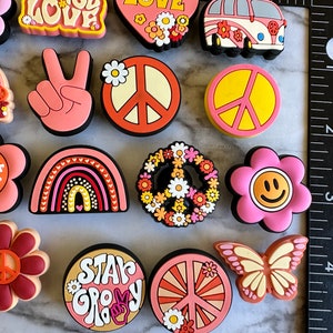 May include: A set of 12 colorful, peace-themed shoe charms. The charms feature peace signs, flowers, rainbows, and the words "Peace Love" and "Star Groovy".