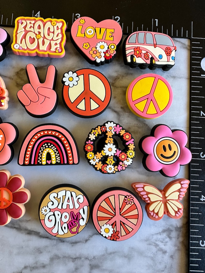 May include: A set of 12 colorful, peace-themed shoe charms. The charms feature peace signs, flowers, rainbows, and the words "Peace Love" and "Star Groovy".