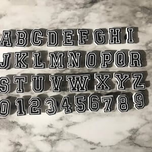 May include: White plastic letters and numbers with black outlines. The letters are in uppercase and the numbers are in a standard font. The letters are arranged in alphabetical order and the numbers are arranged in numerical order.