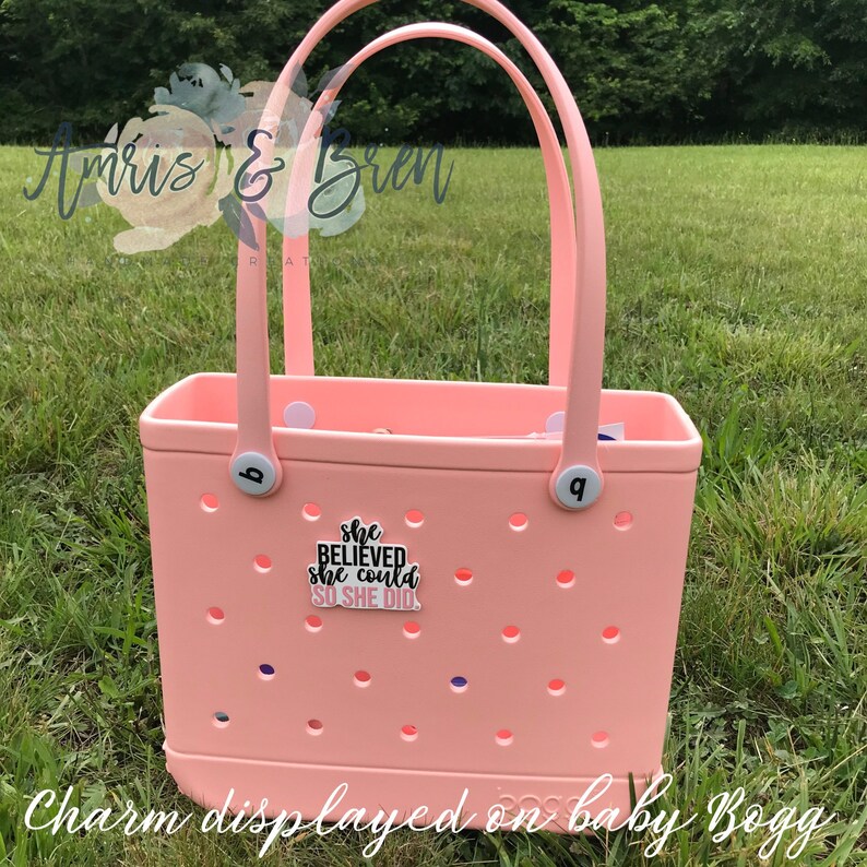 May include: A pink tote bag with a white handle and a black charm that says "She Believed She Could So She Did".