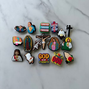 May include: A collection of 15 colorful religious charm charms featuring images of Jesus, Mary, crosses, and inspirational phrases like "Forgiven", "Faith over Fear", "God is my Strength", and "Trust God".