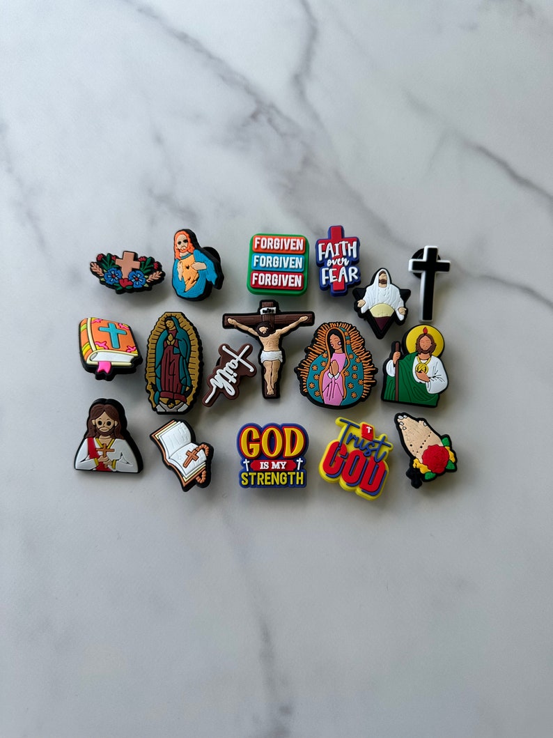 May include: A collection of 15 colorful religious charm charms featuring images of Jesus, Mary, crosses, and inspirational phrases like "Forgiven", "Faith over Fear", "God is my Strength", and "Trust God".