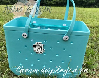 May include: A turquoise blue tote bag with white polka dot lining and white buttons. The bag has a charm attached that says "Stay Humble Hustle Hard".