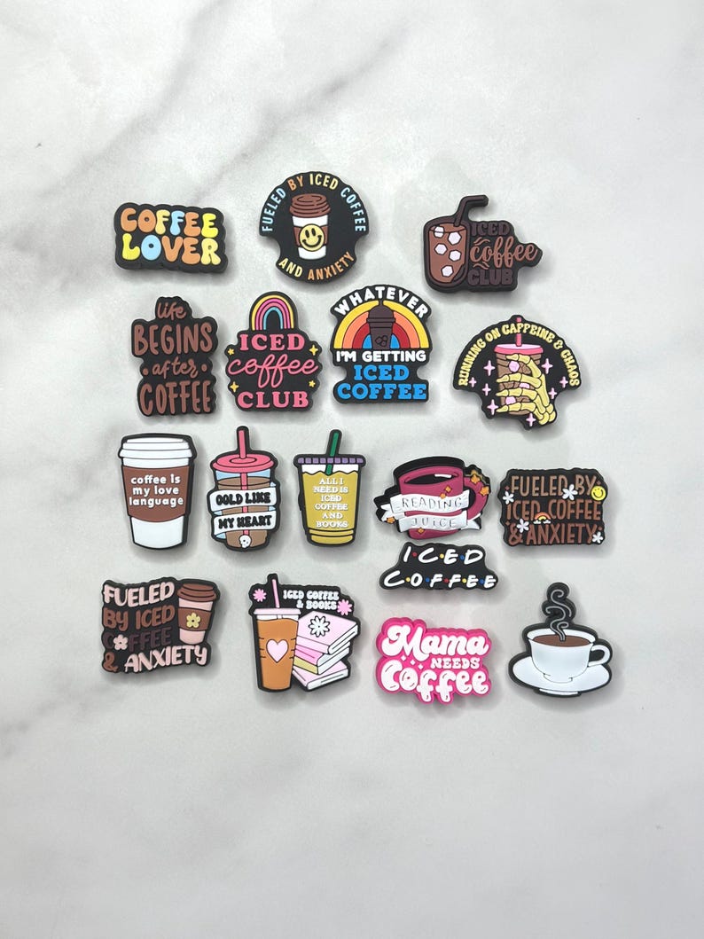 May include: A collection of colorful coffee-themed charms with various phrases like "Coffee Lover," "Iced Coffee Club," and "Mama Needs Coffee." The charms feature coffee cups, rainbows, and books, perfect for personalization.
