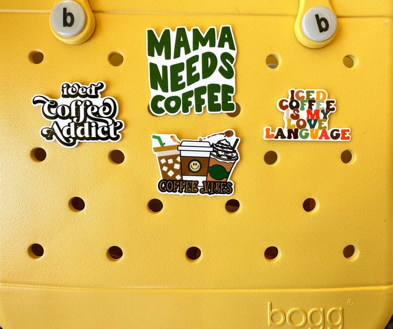 K&ouml;nnte beinhalten: Gelbe Plastikt&uuml;te mit verschiedenen Kaffee-Aufklebern. Die Aufkleber zeigen S&auml;tze wie "Mama Needs Coffee", "Iced Coffee is My Love Language" und "Iced Coffee Addict".
