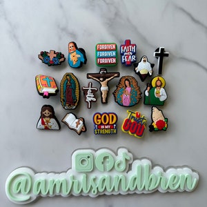 May include: A collection of colorful religious themed shoe charms featuring images of Jesus, Mary, crosses, and bible verses. The charms include phrases like "Forgiven", "Faith over Fear", "God is my Strength", and "Trust God".