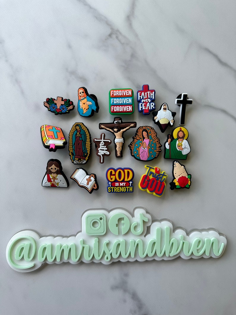 May include: A collection of colorful religious themed shoe charms featuring images of Jesus, Mary, crosses, and bible verses. The charms include phrases like "Forgiven", "Faith over Fear", "God is my Strength", and "Trust God".