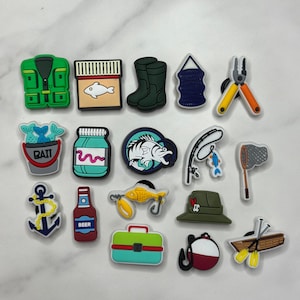 May include: A collection of colorful fishing-themed charms. Includes a green vest, a box with a fish, green boots, a blue net, pliers, a bucket of fish with "BAIT" text, a jar, a fish, a fishing rod, a net, an anchor, a beer bottle, a fish hook, a tackle box, a hat, a bobber, and a boat.