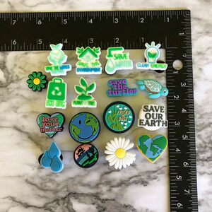 May include: A collection of 14 colorful shoe charms with various environmental themes. The charms feature images of flowers, turtles, hearts, water drops, a lightbulb, a house, a tree, and the Earth. The charms also include text such as "Save the Turtles", "Save Our Earth", "Love Your Mother", and "Friend to Bugs".