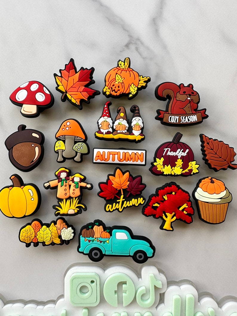 Op de afbeelding: Een verzameling van 17 kleurrijke herfst-schoencharms, waaronder pompoenen, bladeren, paddenstoelen, een eekhoorn, een kabouter, een vogelverschrikker, een vrachtwagen en een cupcake. De charms zijn gemaakt van siliconen en hebben een verscheidenheid aan herfstkleuren, waaronder oranje, rood, geel, bruin en groen.