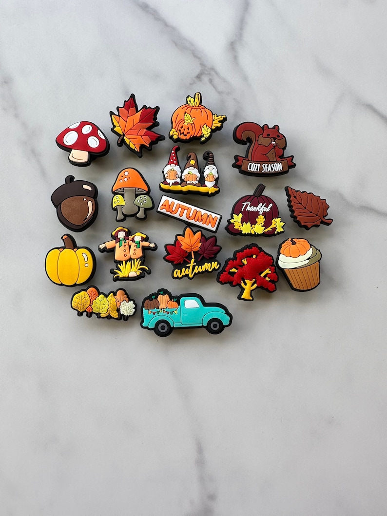 Op de afbeelding: Een verzameling van 17 herfst-thema schoencharms, waaronder pompoenen, bladeren, eikels, een vrachtwagen, een eekhoorn, gnomen en een vogelverschrikker. De charms zijn gemaakt van kleurrijk rubber en hebben herfstkleuren zoals oranje, rood, bruin en geel.