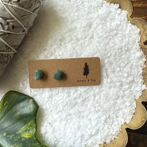 May include: A pair of green gemstone earrings on a brown card with the text "forest & fog".