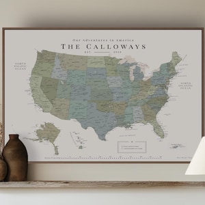 Peut inclure: Une carte murale encadrée des États-Unis intitulée Our Adventures in America The Calloways Est. 2024. La carte présente des tons sourds de vert, bleu et beige avec les frontières des États, les villes et les noms des océans Pacifique et Atlantique.