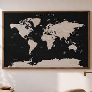 Pode incluir: Um mapa-múndi emoldurado com fundo preto e continentes bege. O mapa está rotulado como "WORLD MAP" em texto branco. A moldura é de cor castanha quente. O mapa está pendurado numa parede branca.